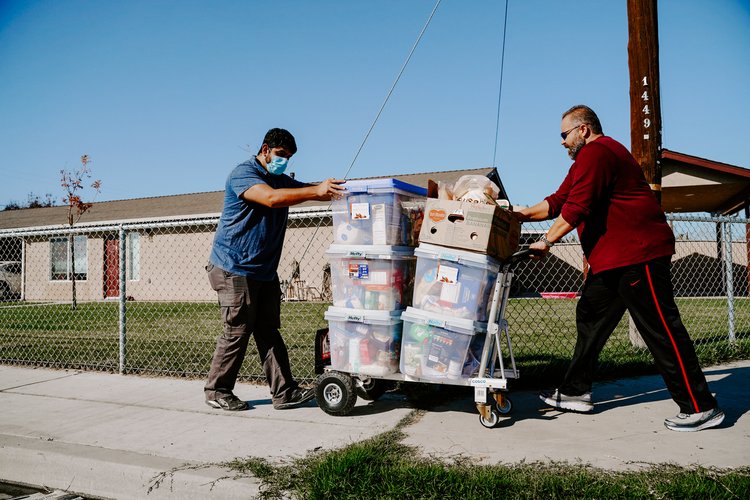 Multiple bins of food being pushed on a hand truck